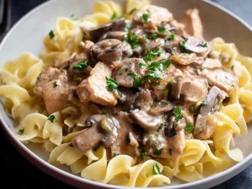 Creamy Chicken Stroganoff served over egg noodles in a white bowl garnished with fresh parsley
