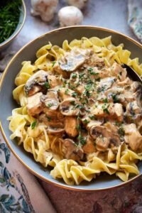 Creamy Chicken Stroganoff served over egg noodles in a white bowl garnished with fresh parsley