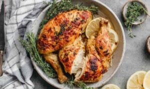 Chicken under a brick in a large cast-iron skillet with golden crispy skin, whole garlic cloves, and fresh thyme sprigs after roasting