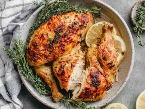 Chicken under a brick in a large cast-iron skillet with golden crispy skin, whole garlic cloves, and fresh thyme sprigs after roasting