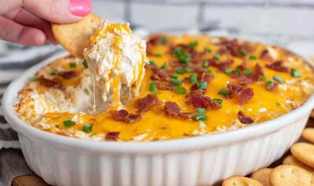 Crack Chicken Dip baked in a white dish with melted cheese, crispy bacon, and green onions on top
