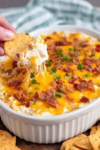 Crack Chicken Dip baked in a white dish with melted cheese, crispy bacon, and green onions on top
