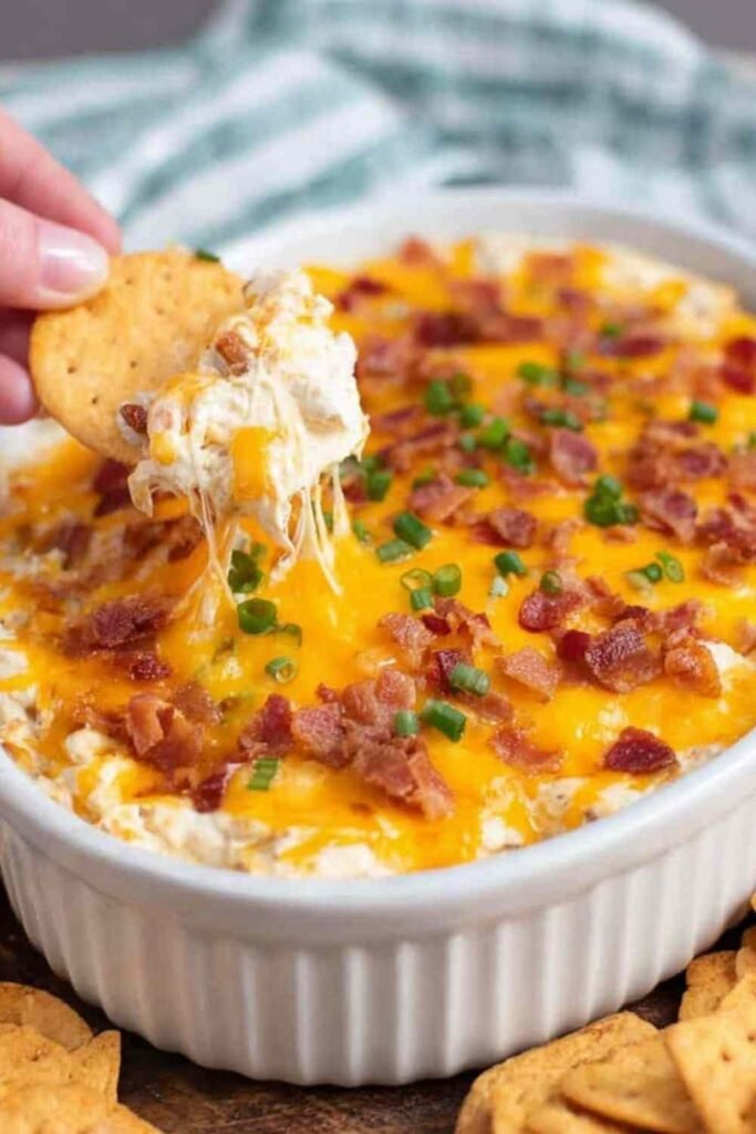 Crack Chicken Dip baked in a white dish with melted cheese, crispy bacon, and green onions on top