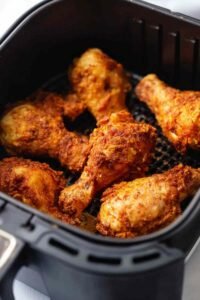 Crispy air fryer fried chicken drumsticks arranged in a single layer inside an air fryer basket, golden skin seasoned with smoked paprika and chili powder