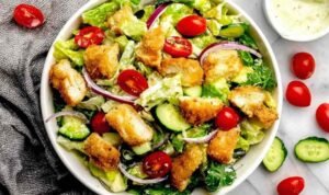 Crispy chicken tender salad recipe in a white bowl with romaine lettuce, avocado, cherry tomatoes, and honey mustard dressing