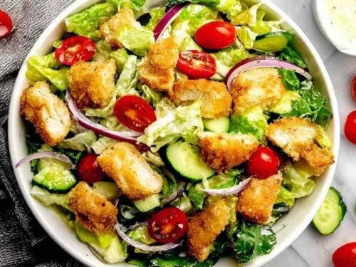 Crispy chicken tender salad recipe in a white bowl with romaine lettuce, avocado, cherry tomatoes, and honey mustard dressing