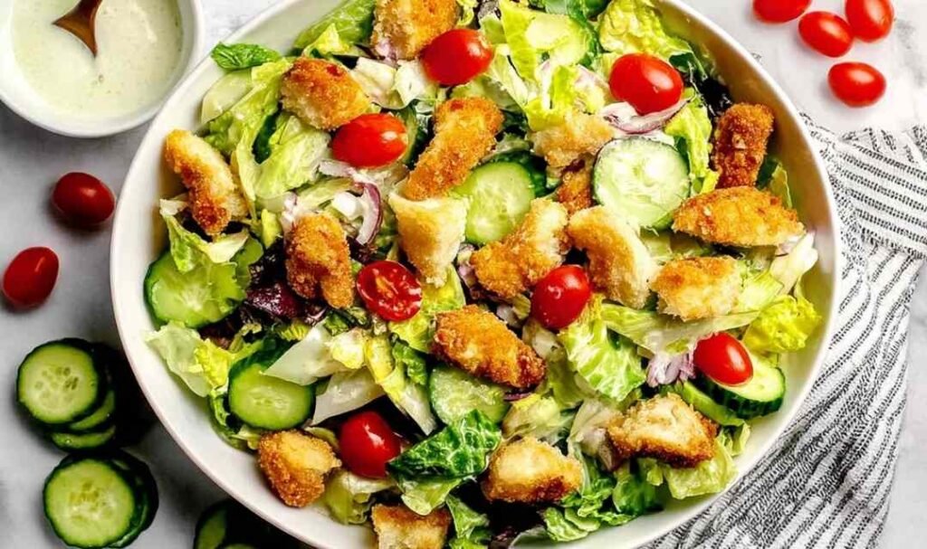 Crispy chicken tender salad recipe in a white bowl with romaine lettuce, avocado, cherry tomatoes, and honey mustard dressing