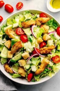 Crispy chicken tender salad recipe in a white bowl with romaine lettuce, avocado, cherry tomatoes, and honey mustard dressing