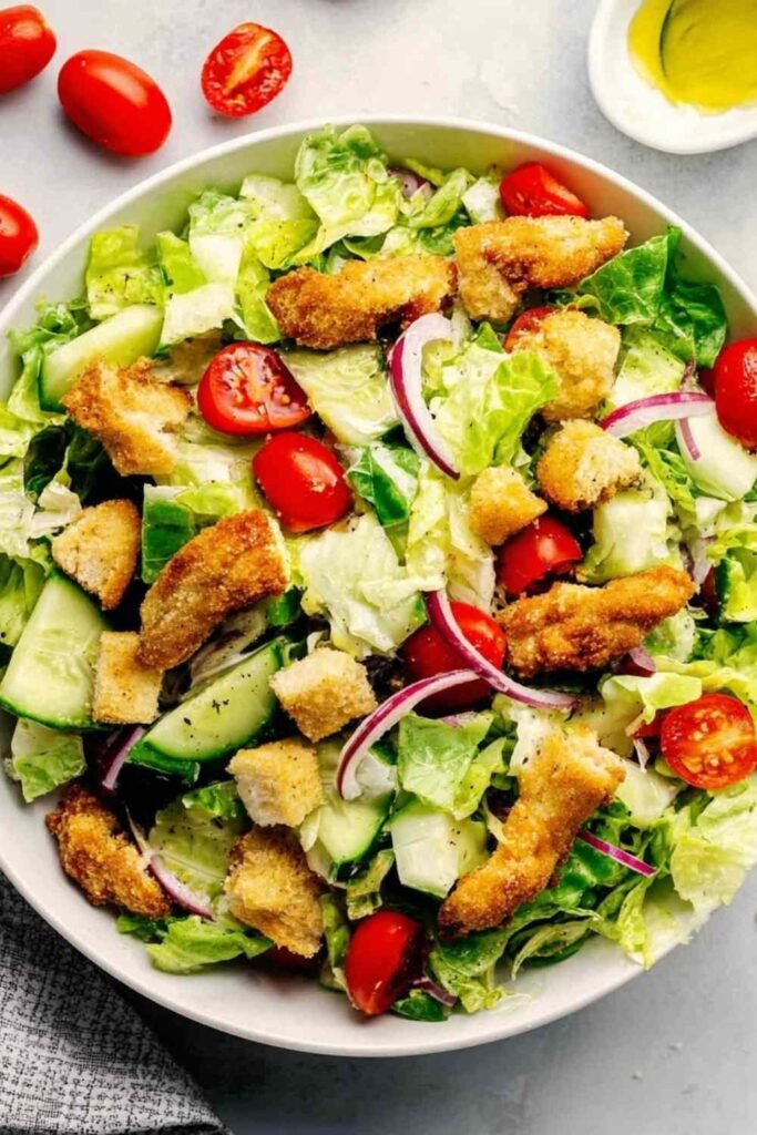 Crispy chicken tender salad recipe in a white bowl with romaine lettuce, avocado, cherry tomatoes, and honey mustard dressing