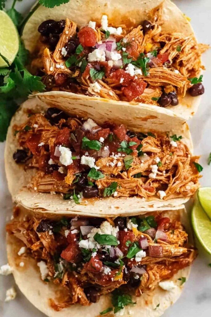 Close-up of crockpot chicken tacos filled with shredded chicken, black beans, and corn in flour tortillas garnished with fresh cilantro