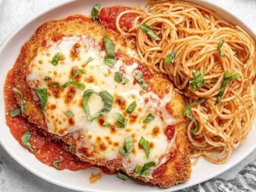 Healthy Baked Chicken Parmesan cutlets on a baking sheet with bubbly melted mozzarella and marinara sauce fresh from the oven