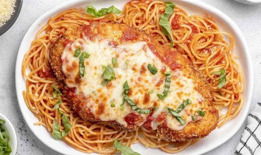 Healthy Baked Chicken Parmesan cutlets on a baking sheet with bubbly melted mozzarella and marinara sauce fresh from the oven
