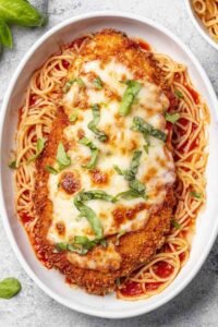 Healthy Baked Chicken Parmesan cutlets on a baking sheet with bubbly melted mozzarella and marinara sauce fresh from the oven