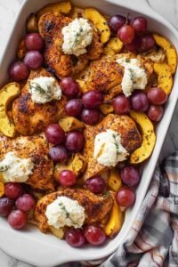 Herb roasted chicken with grapes, acorn squash, and ricotta served in a white baking dish