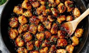 Honey garlic chicken bites in a skillet coated in sticky sweet garlic sauce, garnished with parsley and red chili flakes