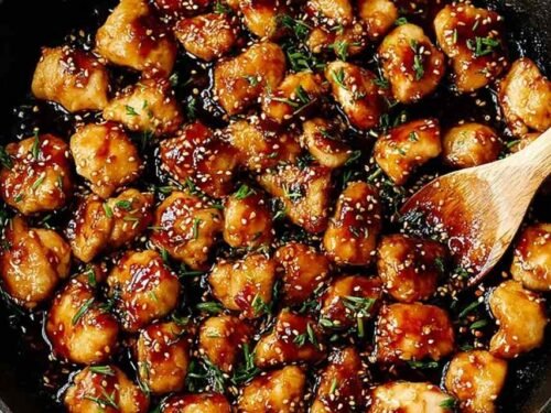 Honey garlic chicken bites in a skillet coated in sticky sweet garlic sauce, garnished with parsley and red chili flakes