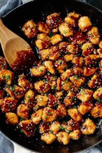 Honey garlic chicken bites in a skillet coated in sticky sweet garlic sauce, garnished with parsley and red chili flakes
