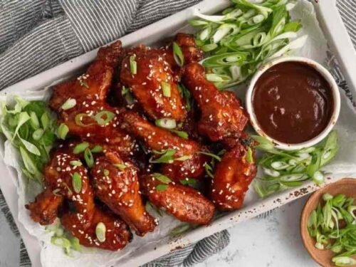 Crispy baked Korean chicken wings on a foil-lined baking sheet brushed with sticky gochujang sauce and topped with sesame seeds and green onions