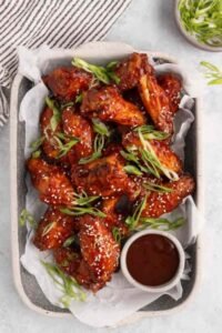 Crispy baked Korean chicken wings on a foil-lined baking sheet brushed with sticky gochujang sauce and topped with sesame seeds and green onions