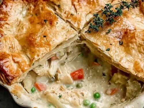 Homemade Old-Fashioned Chicken Pot Pie being assembled in a glass pie dish with creamy chicken vegetable filling and second pie crust being placed on top