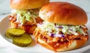 Close-up of a pulled BBQ chicken sandwich with creamy coleslaw and pickles on a toasted bun