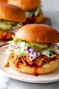 Close-up of a pulled BBQ chicken sandwich with creamy coleslaw and pickles on a toasted bun