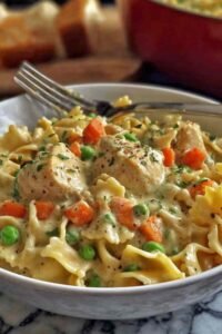 Chicken pot pie pasta in a white bowl with creamy sauce, tender chicken chunks, and mixed vegetables over egg noodles
