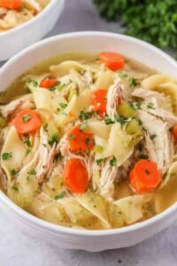 Overhead view of homemade shredded chicken noodle soup with wide egg noodles, carrots, and celery in a Dutch oven