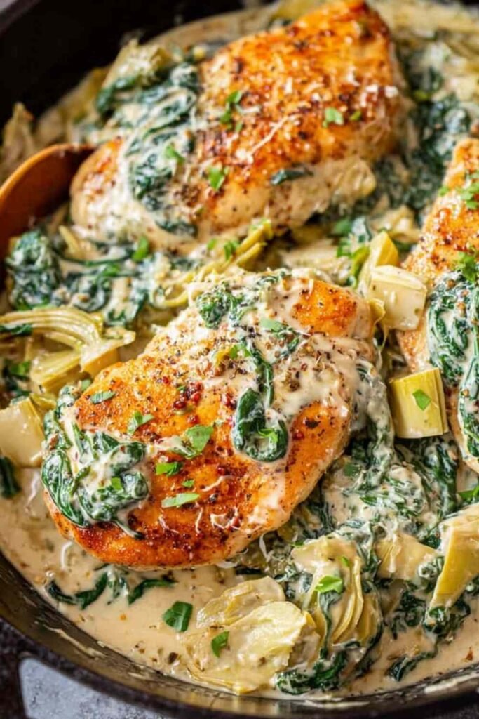 Creamy spinach artichoke chicken in a skillet with Parmesan cheese and wilted spinach