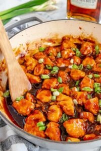 Bourbon chicken in a skillet with sticky sweet and savory sauce garnished with green onions