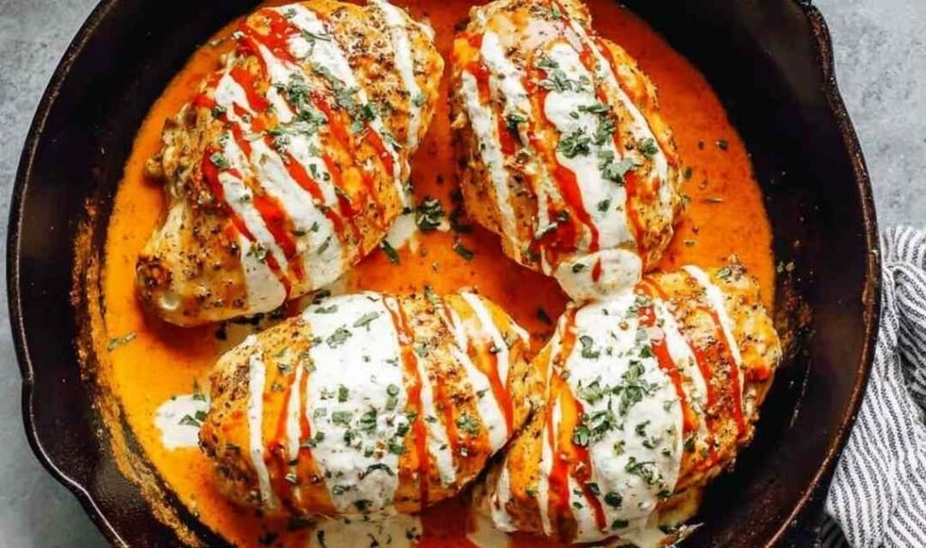 Stuffed Buffalo chicken breast sliced open to reveal creamy cheddar ranch filling, drizzled with ranch and topped with green onions on a white plate