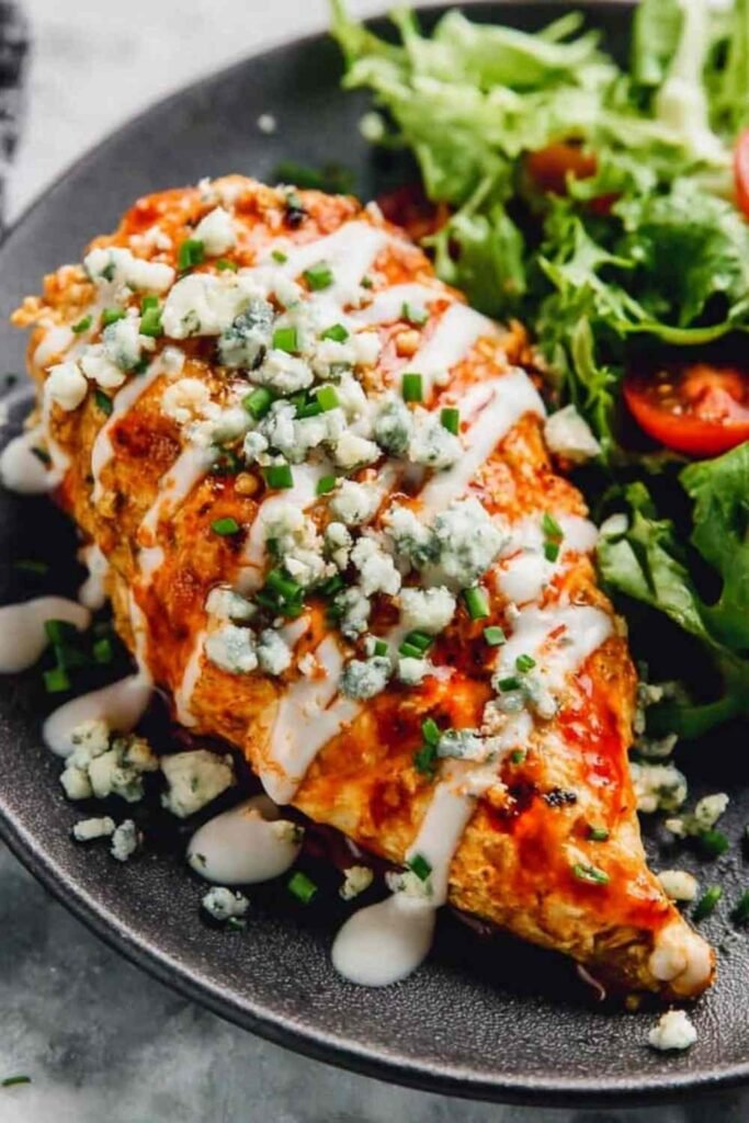 Stuffed Buffalo chicken breast sliced open to reveal creamy cheddar ranch filling, drizzled with ranch and topped with green onions on a white plate